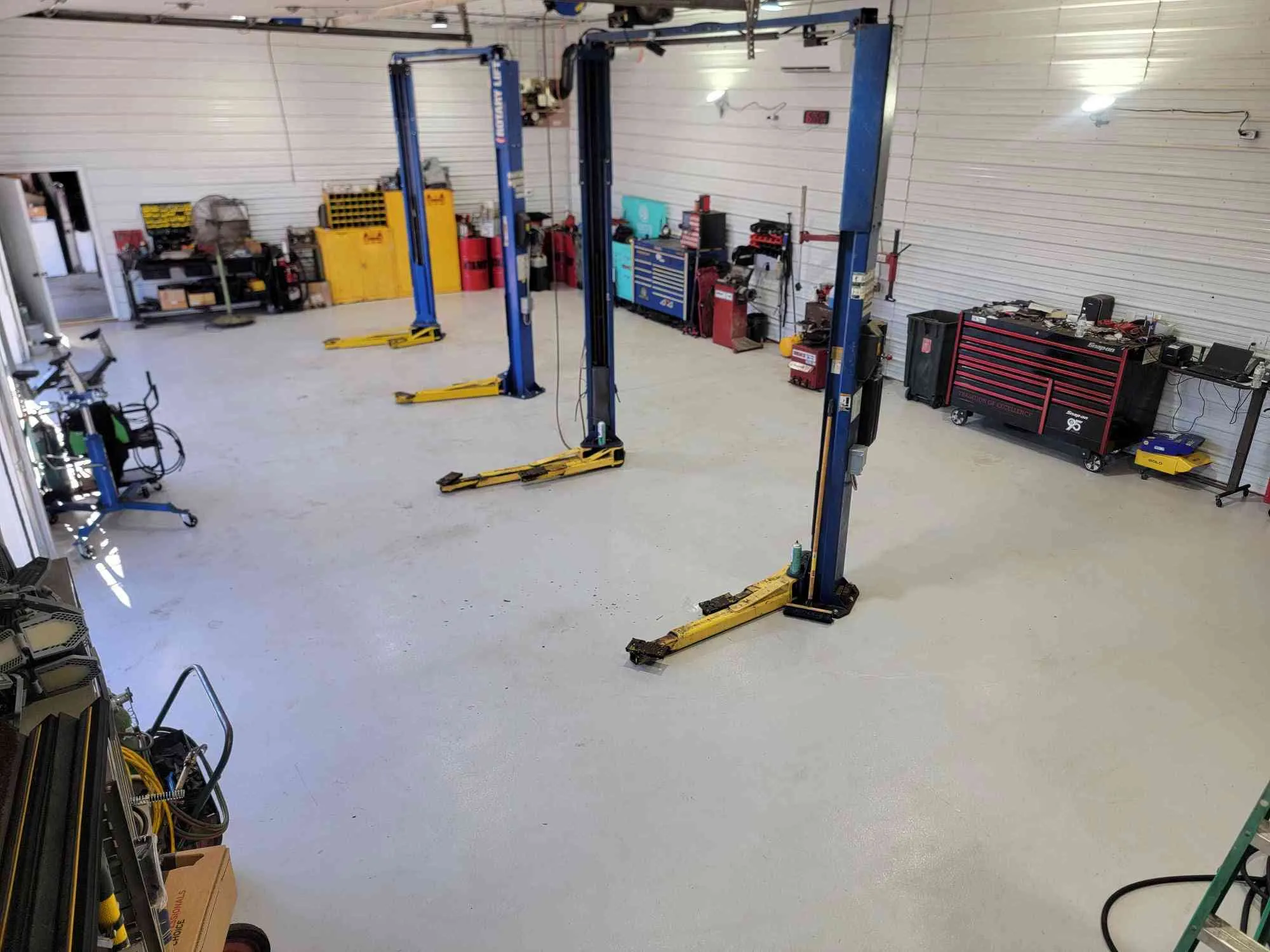 The service bays at the shop: three blue two-post lifts on a clean gray floor, with toolboxes along the walls