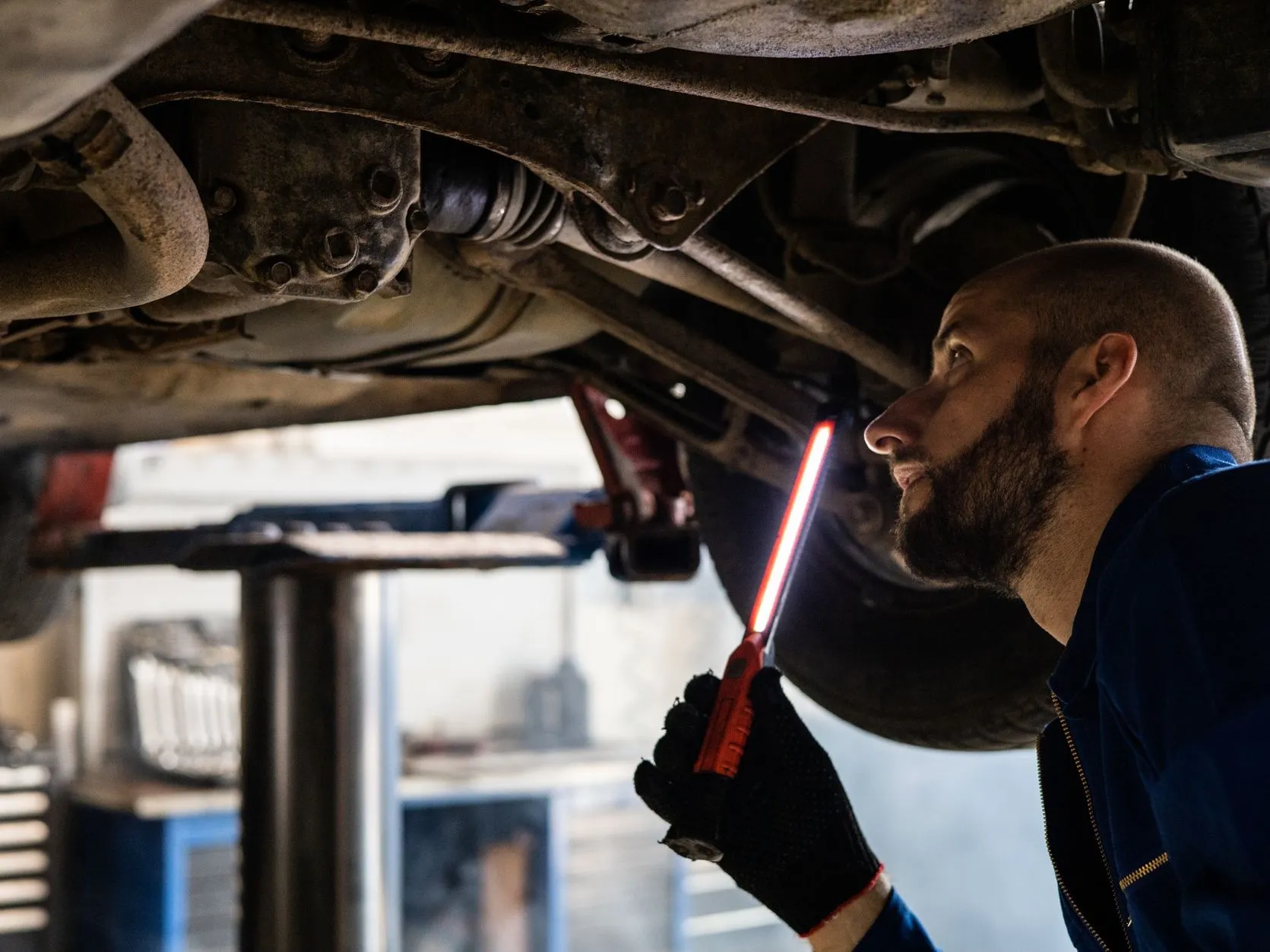 A technician under a car on the lift with a work light
